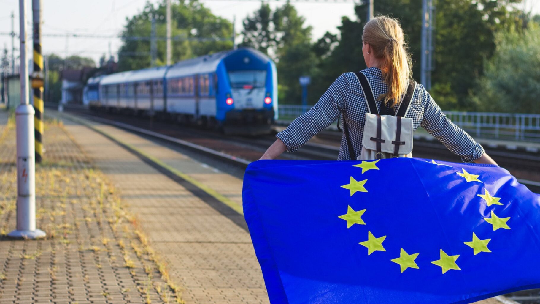 Jeune portant un drapeau europeen sur le quai d'une gare