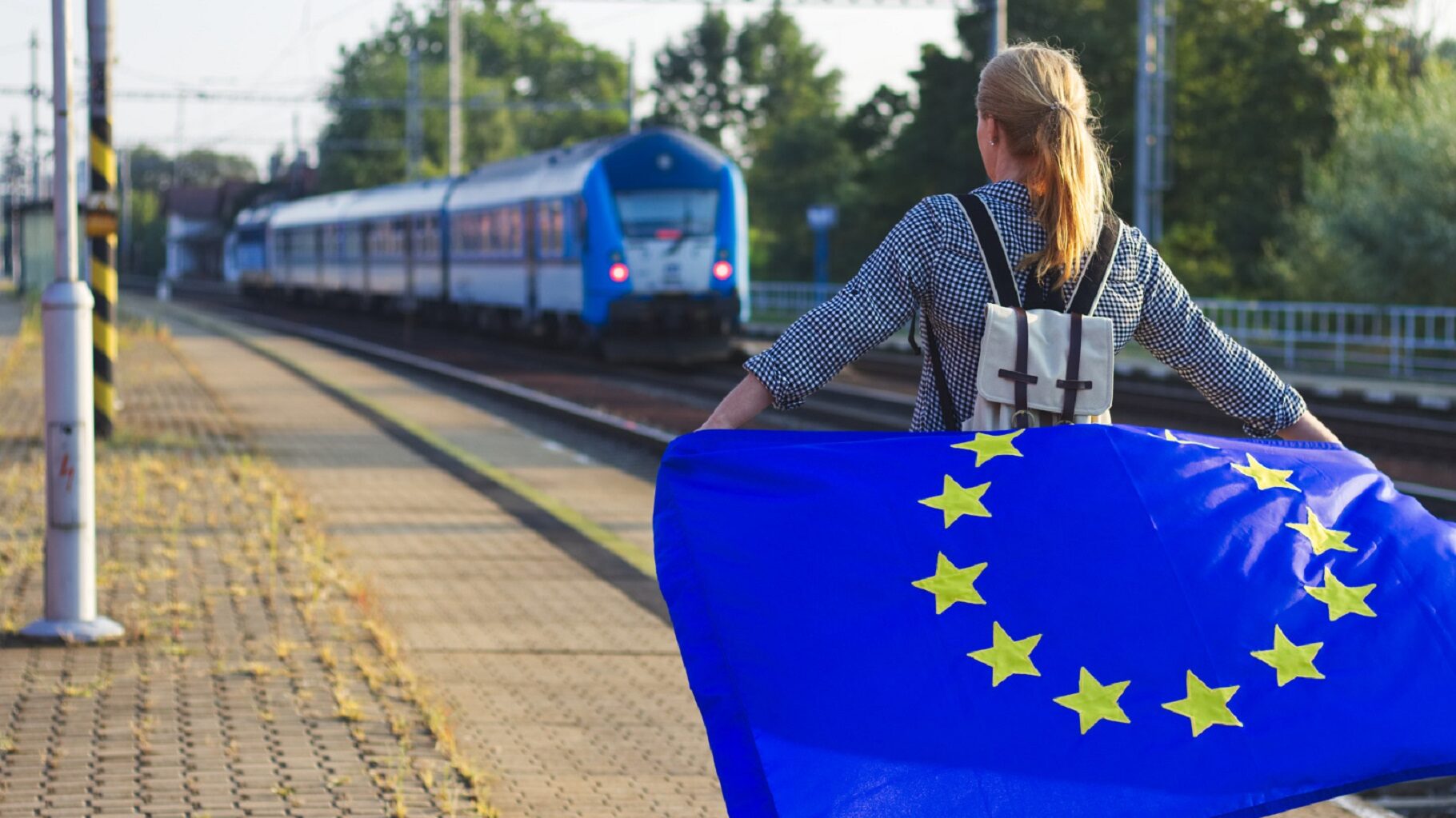 Jeune portant un drapeau europeen sur le quai d'une gare